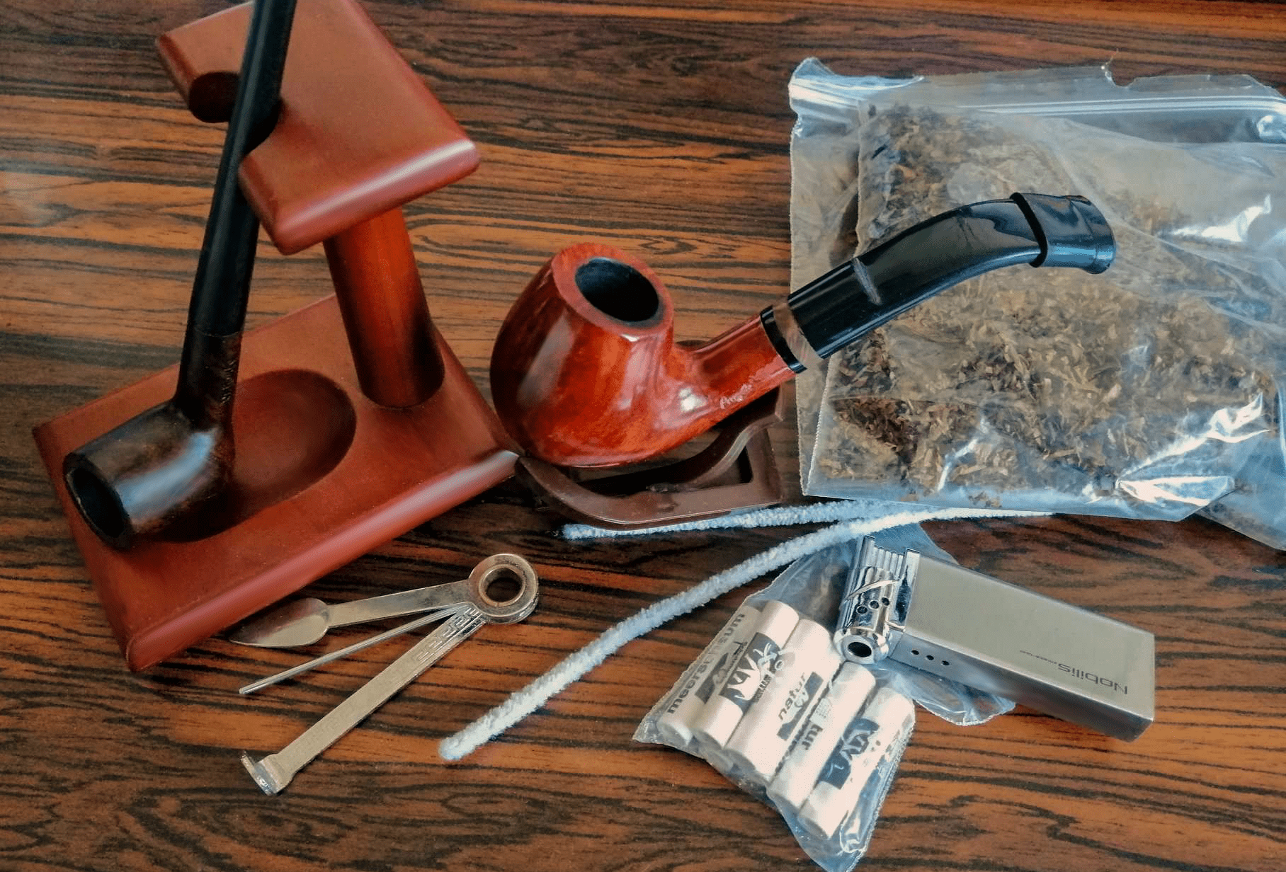 dve drevené briarové fajky a fajkové príslušenstvo položené na stole spolu s tabakom