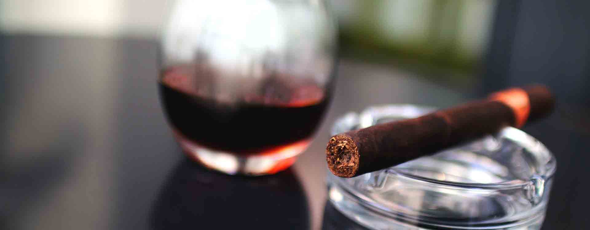 Cigara v cigarovom popolníku a pohár červeného vína
