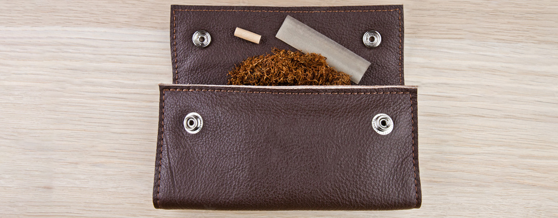 Kožené puzdro na tabak otvorené, kovové cvoky, rozsypaný tabak, cigaretový papierik a filter