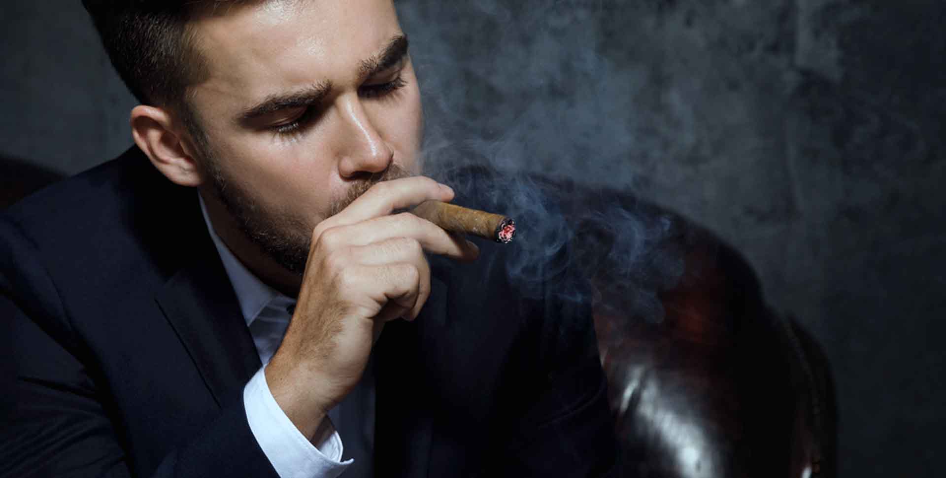 Mladý muž v obleku fajčí cigaru