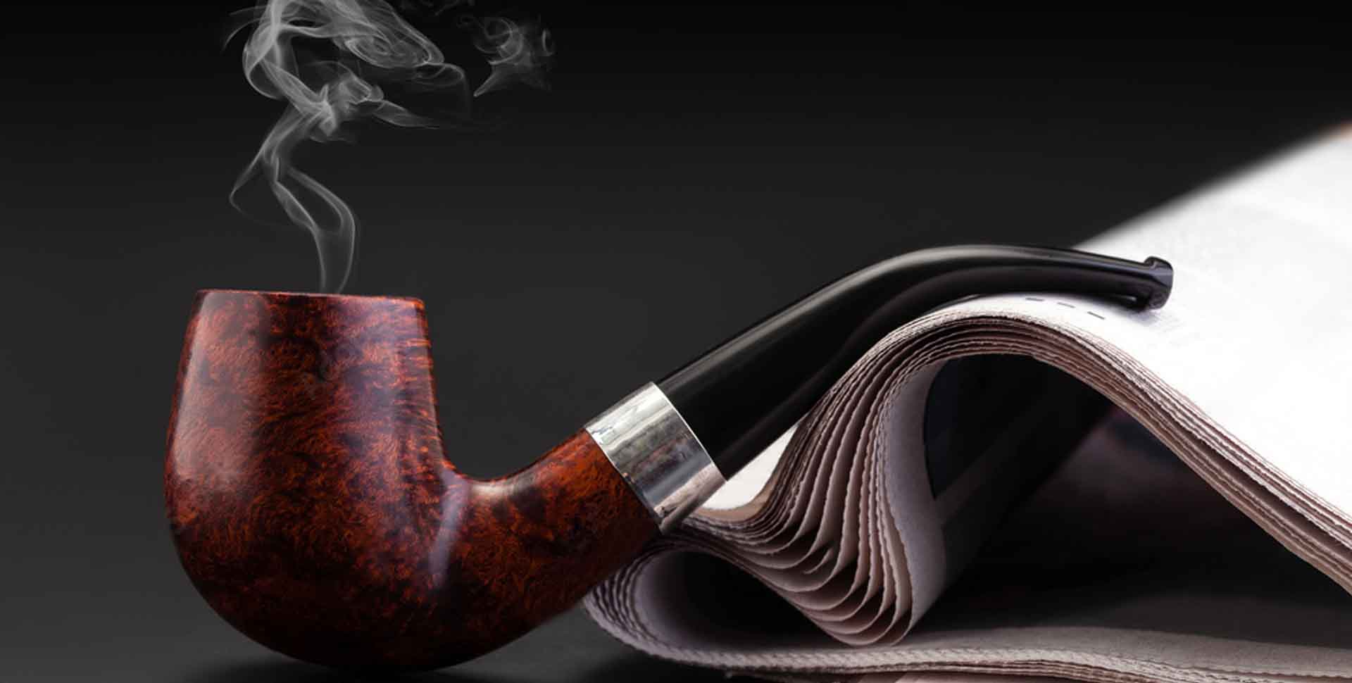 Briarová fajka na tabak, z ktorej sa dymí, položená na zrolovaných novinách