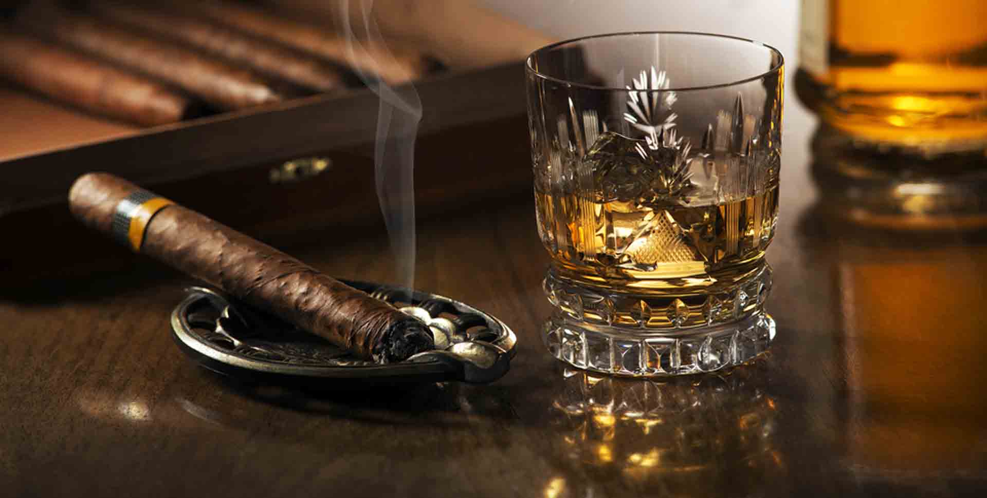 Popolník s odloženou cigarou a pohár whiskey