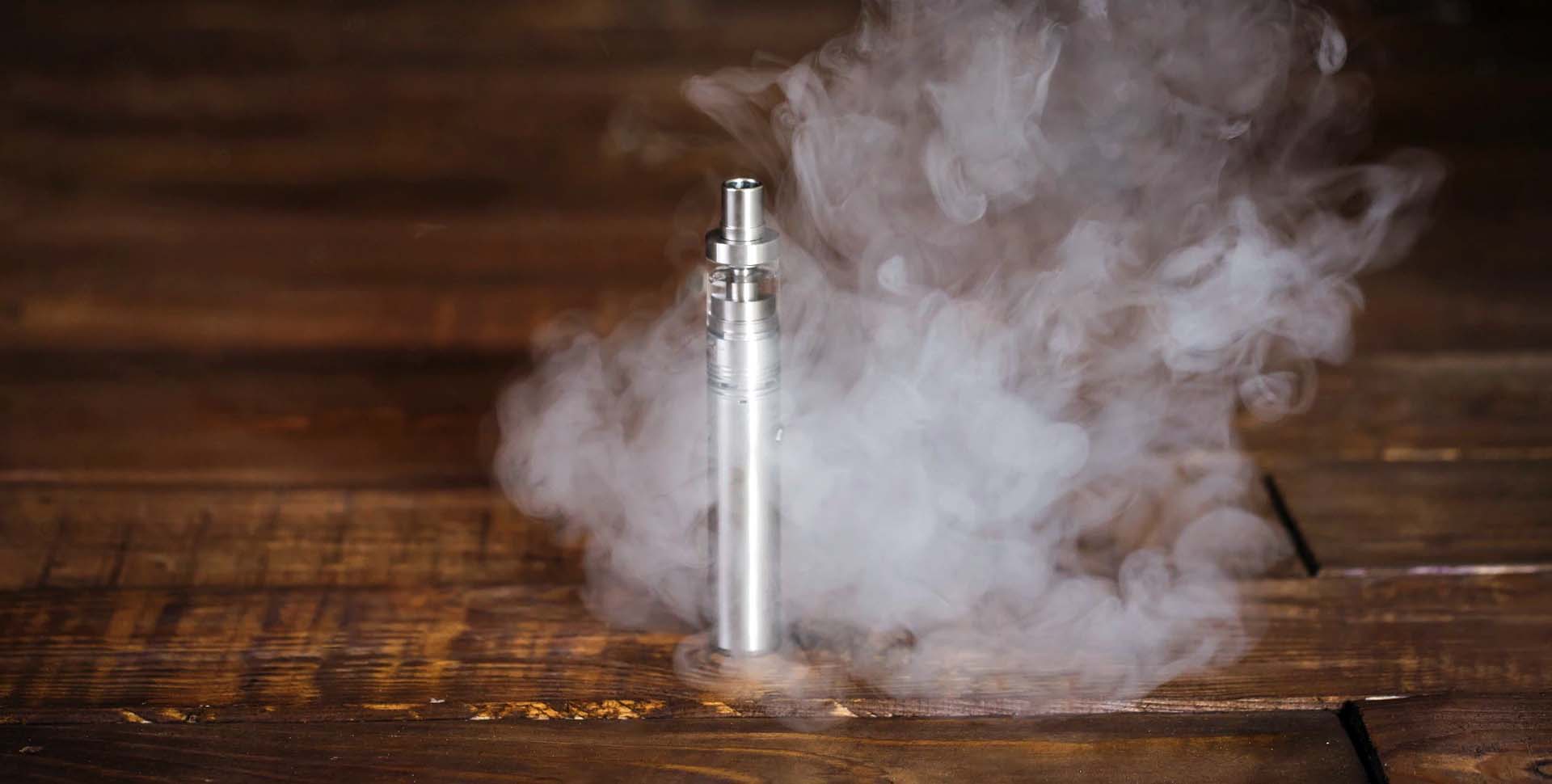 Elektronická cigareta / vaporizér položený na drevenom stole a obklopený dymom